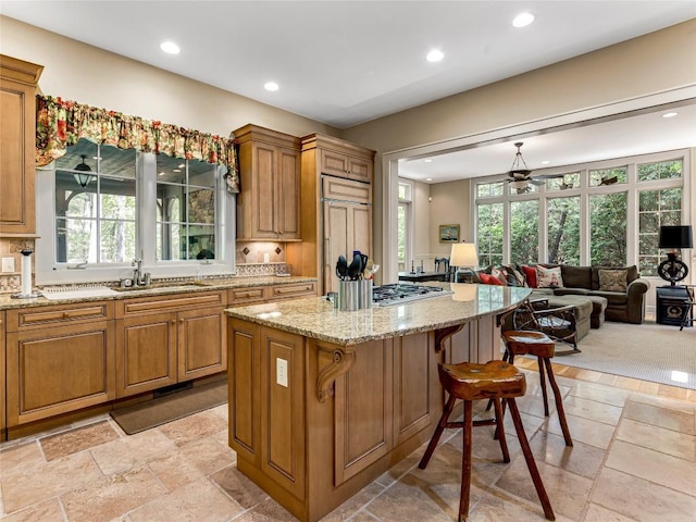 kitchen with light stone counters, brown cabinetry, stainless steel gas cooktop, and stone tile flooring