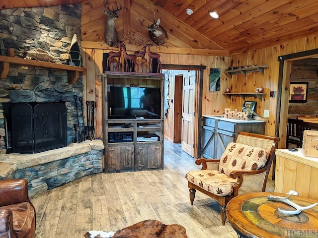 living room with wood ceiling, light hardwood / wood-style flooring, a stone fireplace, vaulted ceiling, and wood walls