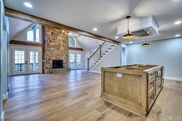 kitchen with a stone fireplace, beam ceiling, wood-type flooring, decorative light fixtures, and french doors