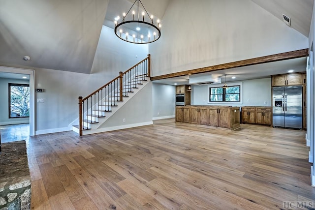 unfurnished living room with an inviting chandelier, high vaulted ceiling, and light hardwood / wood-style floors