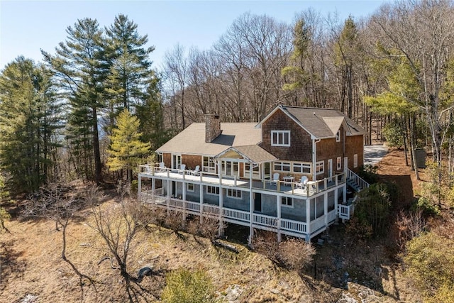 back of property with a balcony, a view of trees, and a chimney