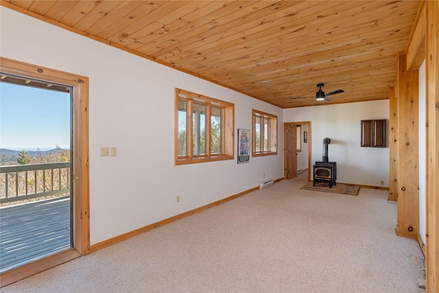 unfurnished living room featuring wooden ceiling, a wood stove, baseboards, and carpet floors