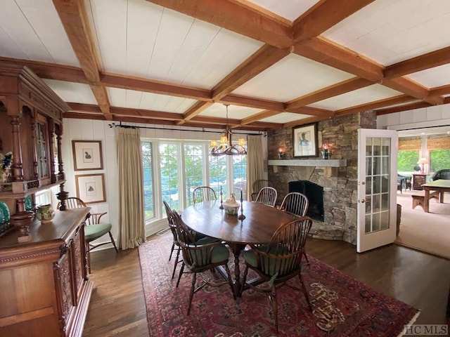 dining room featuring coffered ceiling, dark hardwood / wood-style flooring, a stone fireplace, french doors, and beamed ceiling