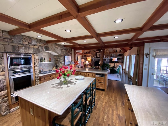 kitchen with dark wood-type flooring, coffered ceiling, a center island, appliances with stainless steel finishes, and beamed ceiling