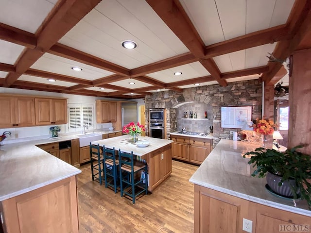 kitchen featuring a kitchen island, sink, stainless steel gas cooktop, beam ceiling, and light hardwood / wood-style flooring