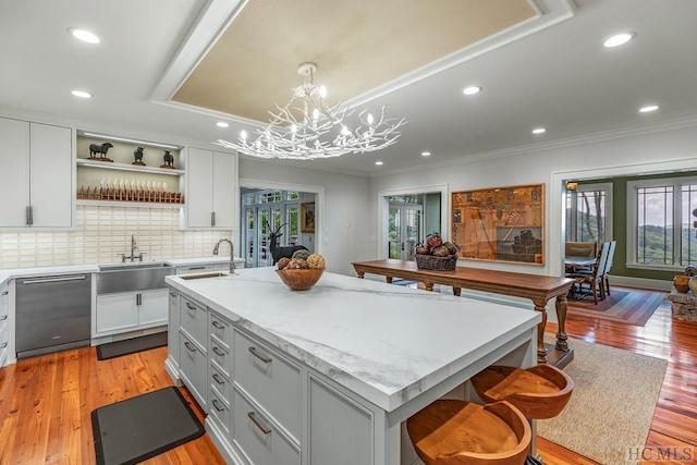 kitchen featuring hanging light fixtures, sink, dishwashing machine, light hardwood / wood-style flooring, and a center island with sink