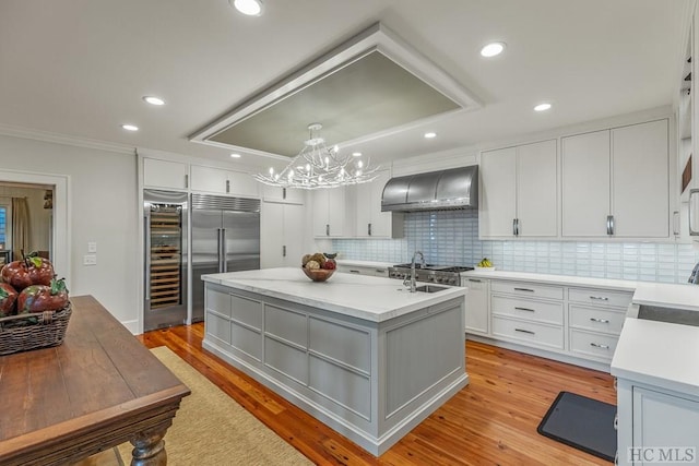 kitchen featuring decorative light fixtures, a center island with sink, white cabinets, and wall chimney range hood