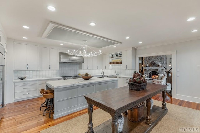 kitchen with white cabinets, extractor fan, a kitchen island, light hardwood / wood-style floors, and hanging light fixtures