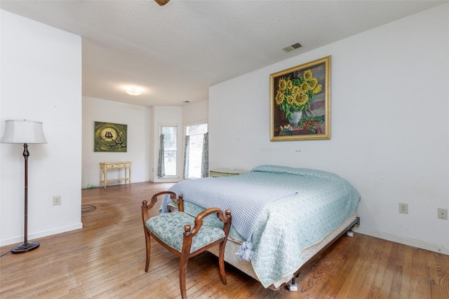 bedroom with a textured ceiling, wood finished floors, visible vents, and baseboards