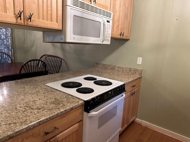 kitchen with light brown cabinetry, white appliances, light stone countertops, and dark hardwood / wood-style floors