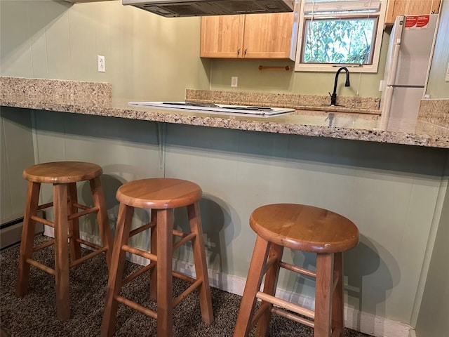 kitchen with white appliances, ventilation hood, light brown cabinets, and a kitchen bar