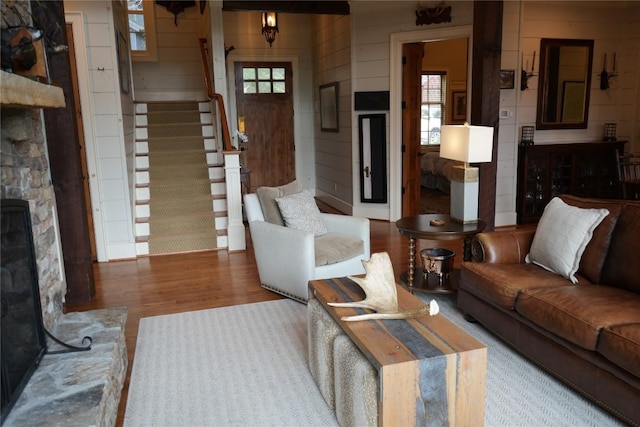 living room with a stone fireplace, a healthy amount of sunlight, stairs, and wood finished floors