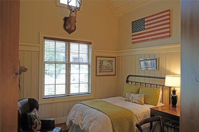bedroom featuring wainscoting, lofted ceiling, and a decorative wall