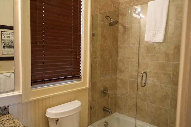 bathroom with toilet, shower / bath combination with glass door, and wainscoting