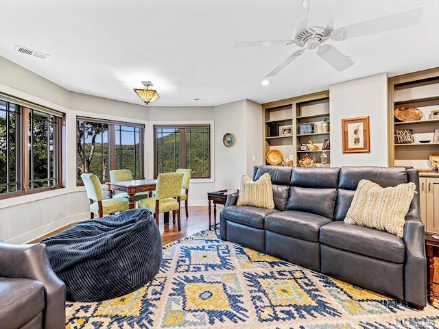 living room with wood-type flooring, built in features, and ceiling fan