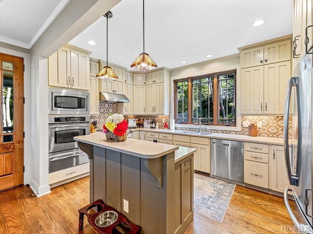 kitchen with pendant lighting, sink, appliances with stainless steel finishes, a center island, and cream cabinetry