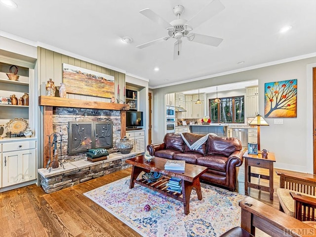 living room with a stone fireplace, built in features, ceiling fan, crown molding, and light hardwood / wood-style flooring