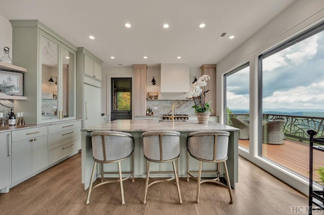 kitchen featuring a breakfast bar, light stone countertops, an island with sink, and light wood-type flooring