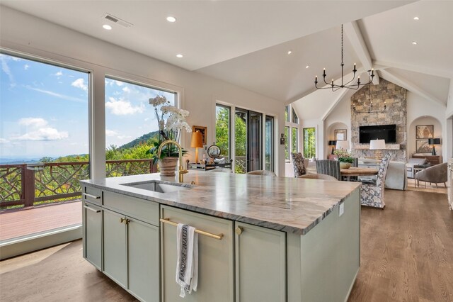 kitchen with a stone fireplace, an island with sink, sink, vaulted ceiling with beams, and a notable chandelier