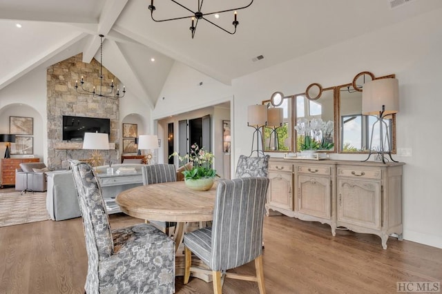 dining area featuring vaulted ceiling with beams, a chandelier, a fireplace, and light hardwood / wood-style floors