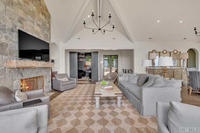 living room featuring beamed ceiling, an inviting chandelier, a stone fireplace, and high vaulted ceiling