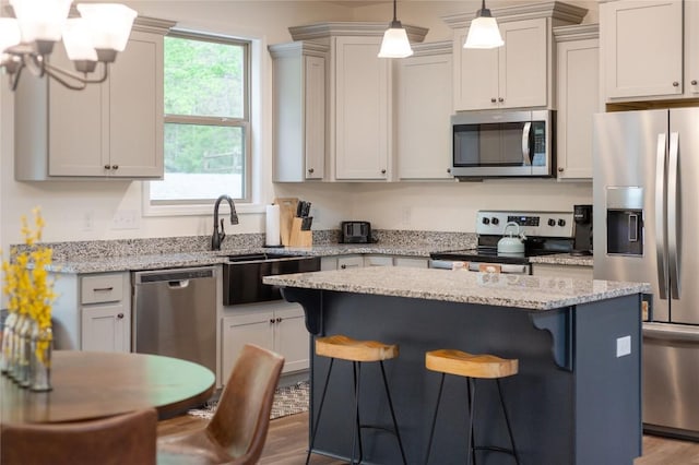 kitchen featuring appliances with stainless steel finishes, a breakfast bar, a center island, wood finished floors, and light stone counters