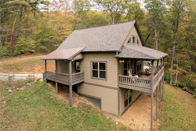 rear view of house featuring a shingled roof, a view of trees, and a lawn