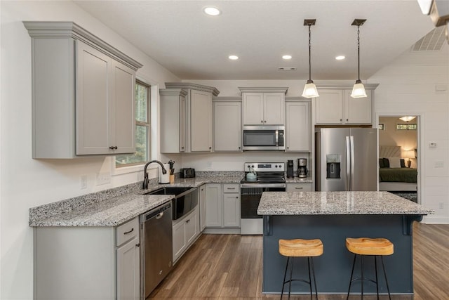 kitchen with appliances with stainless steel finishes, gray cabinets, a sink, a kitchen bar, and wood finished floors