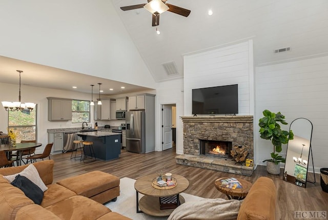 living room featuring hardwood / wood-style flooring, a fireplace, ceiling fan with notable chandelier, and high vaulted ceiling