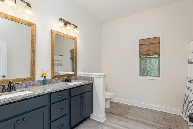 bathroom with wood finished floors, baseboards, double vanity, and toilet