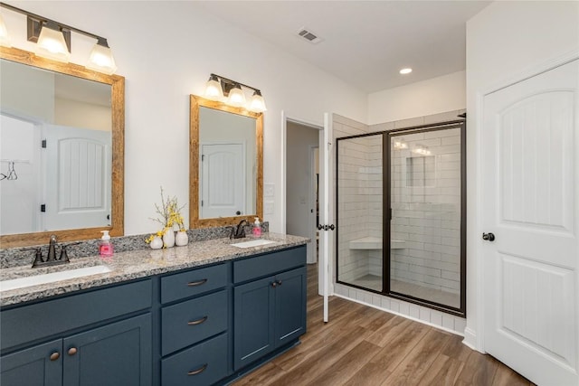 full bathroom featuring wood finished floors, a stall shower, double vanity, and recessed lighting