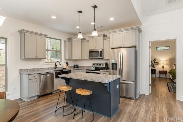 kitchen with a kitchen island, appliances with stainless steel finishes, sink, gray cabinetry, and a kitchen bar