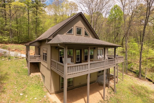 rear view of house with roof with shingles, a yard, a wooded view, a patio area, and a wooden deck