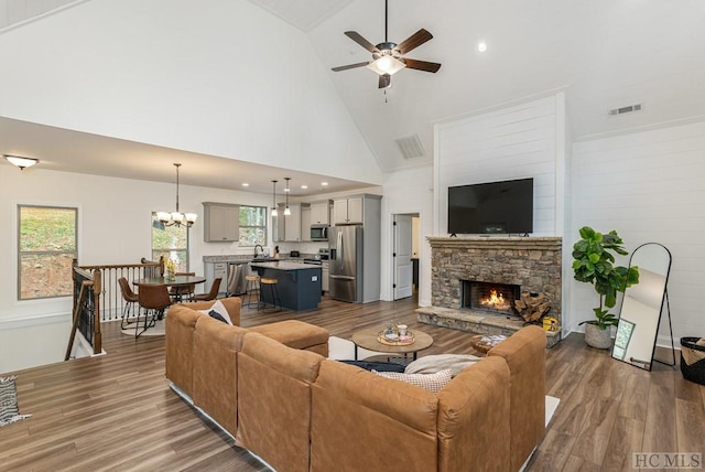 living room with wood-type flooring, ceiling fan with notable chandelier, a fireplace, and high vaulted ceiling