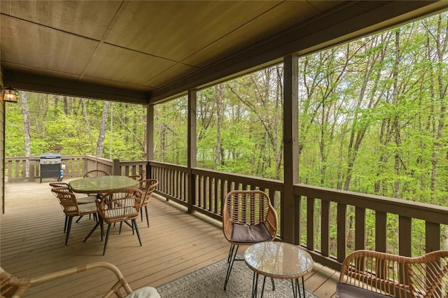 deck featuring outdoor dining area, a view of trees, and a grill