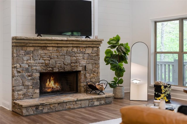 living room featuring wood finished floors, a stone fireplace, and baseboards