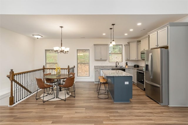 kitchen featuring appliances with stainless steel finishes, gray cabinets, a sink, a kitchen island, and light wood-style floors