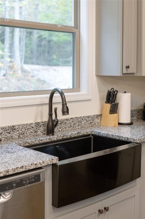 kitchen view of dishwasher, a sink, light stone counters, and white cabinetry