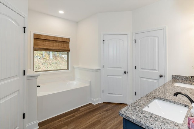 full bathroom with wood finished floors, a bath, double vanity, and recessed lighting