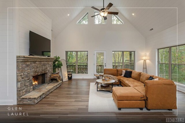 living room featuring ceiling fan, a stone fireplace, a towering ceiling, and dark hardwood / wood-style flooring