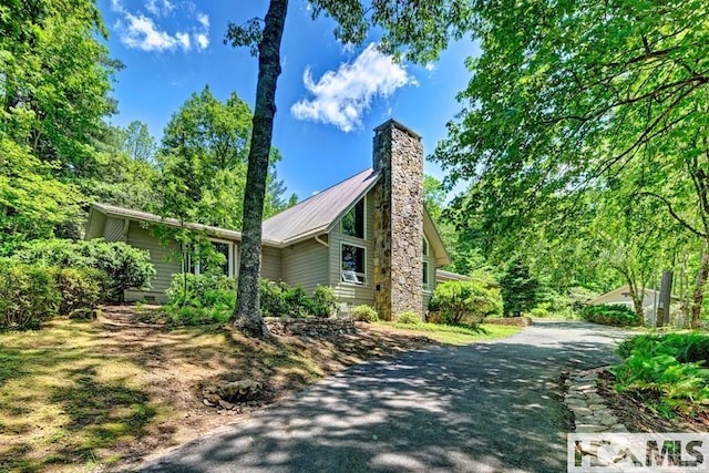 view of property exterior with a chimney, driveway, metal roof, and crawl space