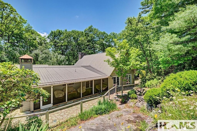 rear view of house featuring a chimney, a sunroom, and metal roof