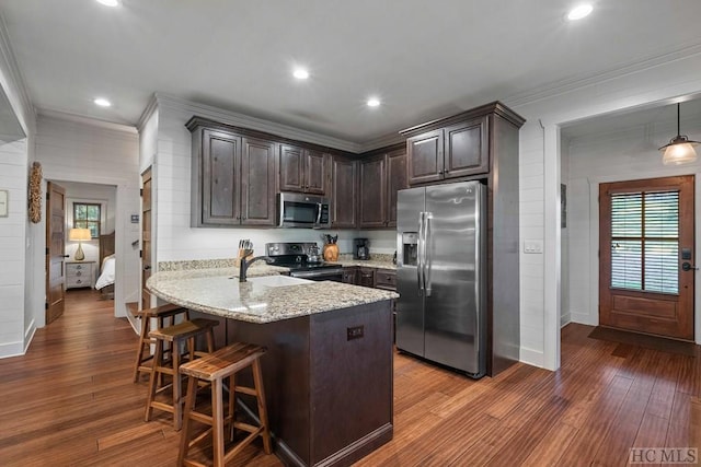 kitchen featuring appliances with stainless steel finishes, a breakfast bar, hanging light fixtures, dark brown cabinetry, and kitchen peninsula