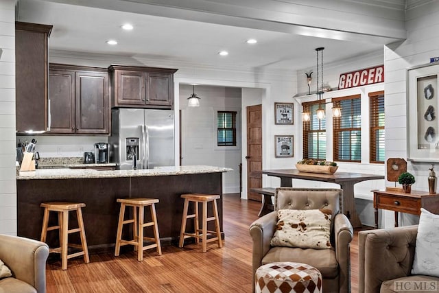 kitchen with stainless steel fridge with ice dispenser, decorative light fixtures, a breakfast bar area, light hardwood / wood-style floors, and light stone counters