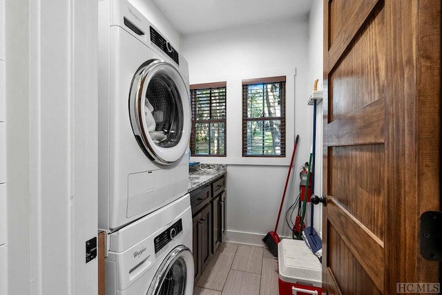 clothes washing area with stacked washing maching and dryer, light tile patterned flooring, and cabinets