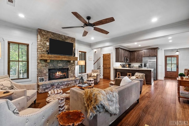 living room featuring dark hardwood / wood-style flooring, a stone fireplace, ornamental molding, and ceiling fan