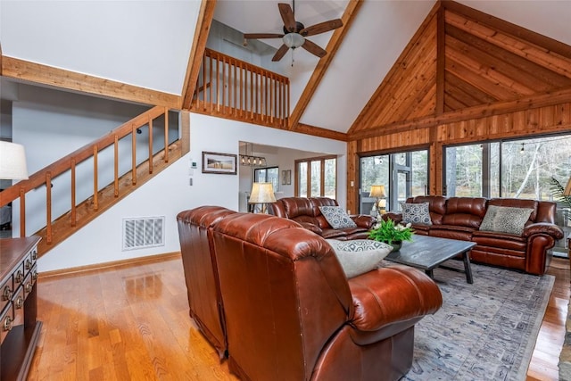 living area featuring visible vents, light wood-style flooring, ceiling fan, stairs, and high vaulted ceiling