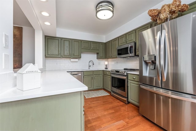 kitchen featuring green cabinets, stainless steel appliances, a sink, and decorative backsplash