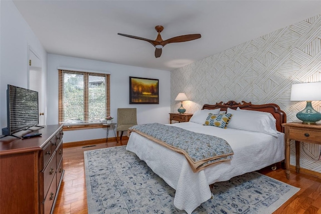 bedroom featuring light wood-style flooring, an accent wall, ceiling fan, baseboards, and wallpapered walls