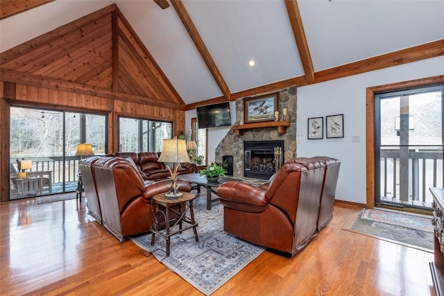 living room featuring light wood finished floors, high vaulted ceiling, a stone fireplace, and beamed ceiling